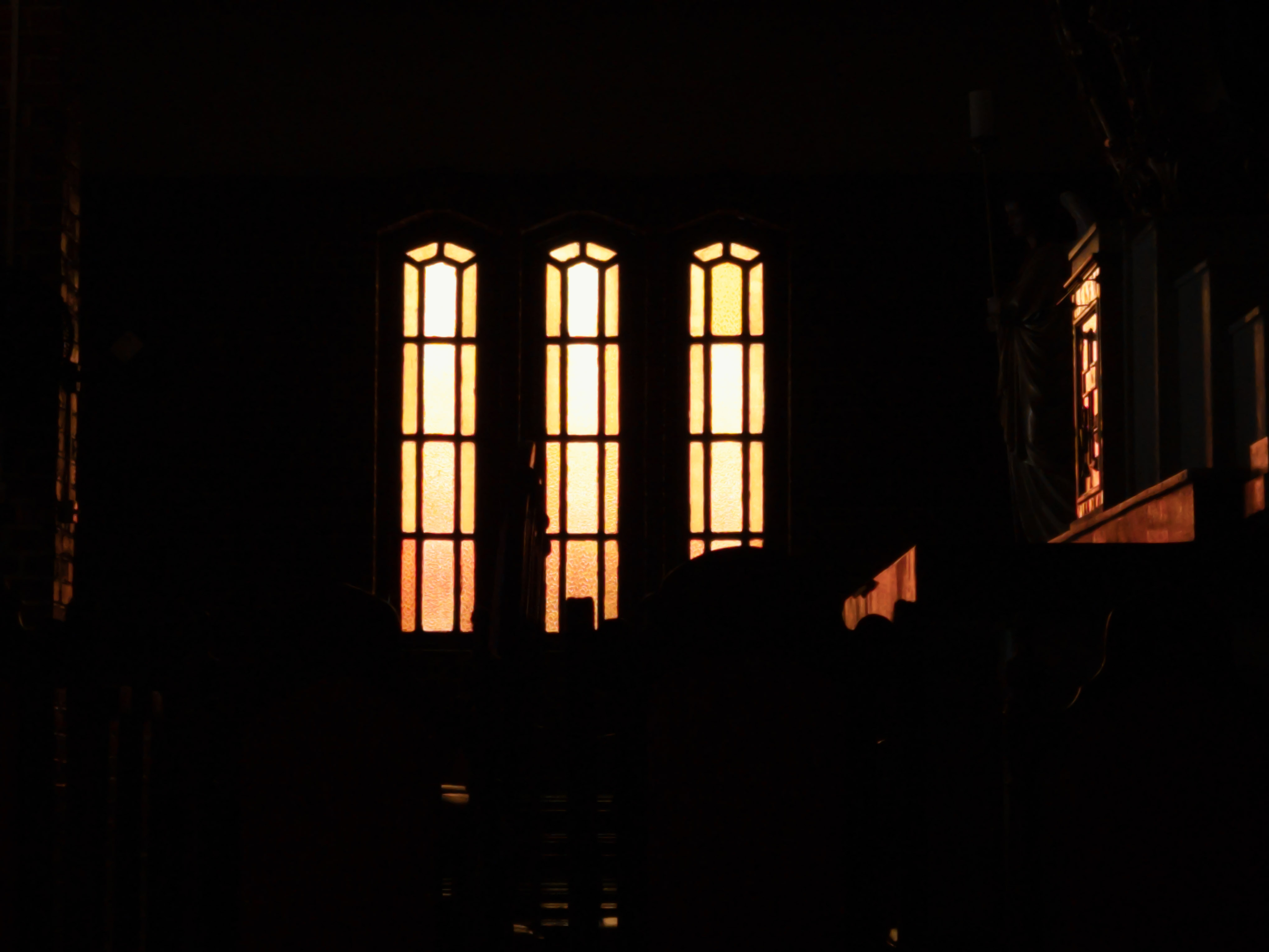 Three arched chapel windows glowing in an otherwise dark interior